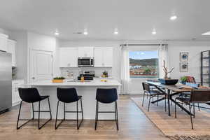 Kitchen featuring a kitchen island with sink, white cabinetry, recessed lighting, light wood finished floors, and a kitchen breakfast bar