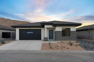 Prairie-style house with stucco siding, concrete driveway, stone siding, a tiled roof, and a garage