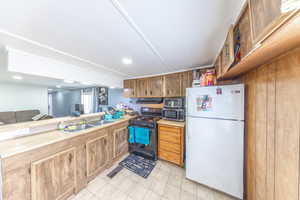 Kitchen featuring freestanding refrigerator, black gas stove, light tile patterned floors, brown cabinetry, and stainless steel microwave