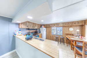 Kitchen featuring a peninsula, light countertops, wood walls, freestanding refrigerator, and brown cabinets