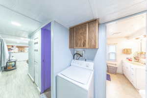 Washroom featuring washer / dryer, light wood-style floors, and cabinet space