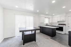 Kitchen featuring white electric stove, dark colored carpet, white cabinetry, recessed lighting, and a peninsula