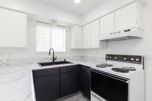 Kitchen with white electric range, white cabinetry, under cabinet range hood, light tile patterned floors, and recessed lighting