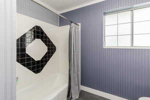 Bathroom featuring wallpapered walls, dark tile patterned floors, shower / bath combo with shower curtain, and ornamental molding
