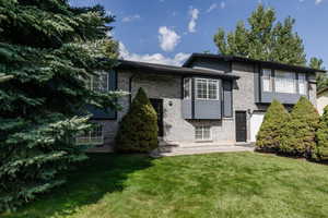 View of front of home with brick siding, a patio area, and a front lawn