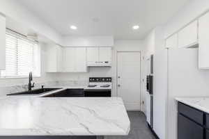 Kitchen featuring white appliances, white cabinetry, a peninsula, dark tile patterned flooring, and light stone countertops