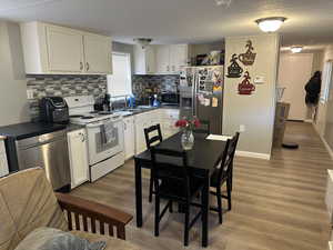 Kitchen featuring stainless steel appliances, dark countertops, white cabinetry, wood finished floors, and a textured ceiling