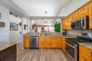 Kitchen with appliances with stainless steel finishes, hanging light fixtures, light granite counters, light wood finished floors, and lofted ceiling