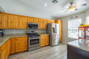 Kitchen featuring granite counters, appliances with stainless steel finishes, vaulted ceiling, a ceiling fan, and LVP floors