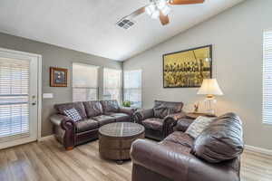 Living room featuring vaulted ceiling, ceiling fan, a textured ceiling, and light wood-style floors