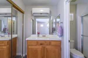 Full bath featuring a vanity, a wall mounted air conditioner and heater , a stall shower, and a textured ceiling