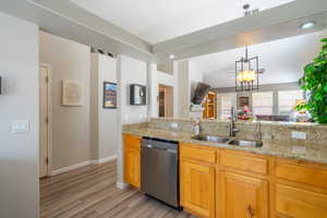 Kitchen withg ranite counters, stainless steel dishwasher, hanging light fixtures, light wood-style floors {LVP}, and open floor plan