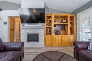 Living room featuring lofted ceiling, a stone fireplace, entertainment center/bookshelves  and LVP floors