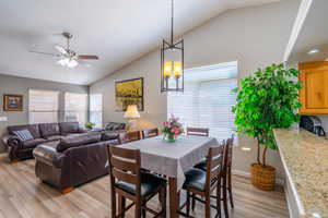 Dining area with light wood-style flooring, vaulted ceiling, a ceiling fan, and a chandelier