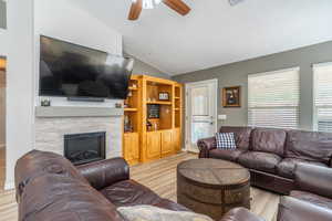 Living room with lofted ceiling, a ceiling fan, an electric fireplace w/ stacked rock surround, light wood finished floors, and a textured ceiling