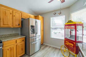 Kitchen with light granite counters, stainless steel fridge with ice dispenser, light LVP flooring, a ceiling fan, and brown cabinets.