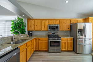 Kitchen withgranite countertops, appliances with stainless steel finishes, vaulted ceiling, recessed lighting, and light LVP flooring