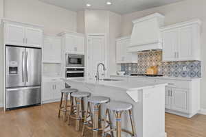 Kitchen featuring appliances with stainless steel finishes, light wood-type flooring, a kitchen bar, tasteful backsplash, and an island with sink