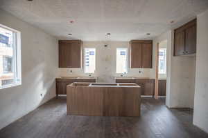Kitchen with a kitchen island, brown cabinetry, dark wood-type flooring, and a textured ceiling