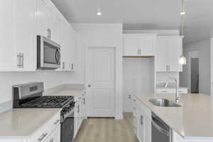 Kitchen featuring appliances with stainless steel finishes, light wood-type flooring, white cabinets, recessed lighting, and pendant lighting