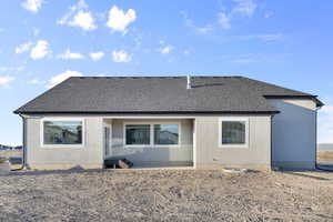 Back of property with a shingled roof, stucco siding, and a patio area