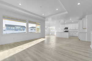 Unfurnished living room featuring a tray ceiling, light wood finished floors, a chandelier, and recessed lighting