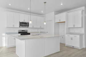 Kitchen with light wood finished floors, range with gas cooktop, stainless steel microwave, white cabinetry, and recessed lighting