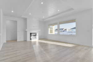 Unfurnished living room featuring a raised ceiling, recessed lighting, a glass covered fireplace, and light wood finished floors