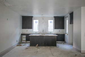 Kitchen with a center island with sink, light countertops, backsplash, and a textured ceiling