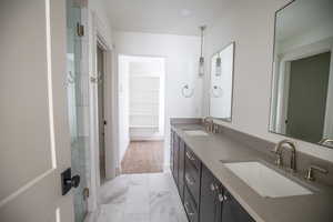 Bathroom with double vanity, a walk in closet, a stall shower, and light marble finish floors