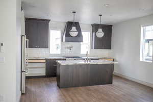 Kitchen featuring dark wood finish cabinets, tasteful backsplash, light stone counters, an island with sink, and a textured ceiling