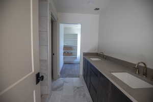 Full bath with double vanity, light marble finish flooring, and a walk in closet