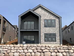 Back of house featuring a patio, a balcony, and stone siding