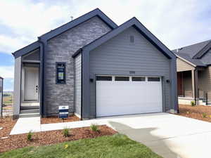 View of front facade featuring stone siding, an attached garage, and concrete driveway