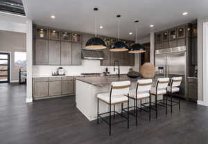 Kitchen with stainless steel built in fridge, glass insert cabinets, a kitchen bar, under cabinet range hood, and hanging light fixtures