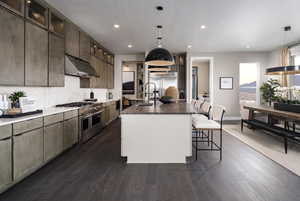 Kitchen featuring recessed lighting, premium appliances, under cabinet range hood, a breakfast bar area, and a center island with sink