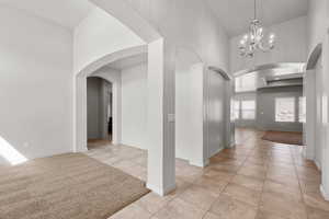 Hallway with a chandelier, light tile patterned floors, arched walkways, and a towering ceiling