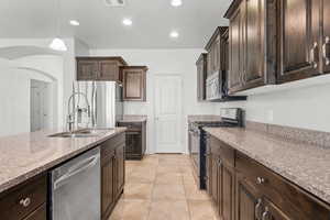 Kitchen with dark brown cabinetry, hanging light fixtures, appliances with stainless steel finishes, recessed lighting, and light stone countertops