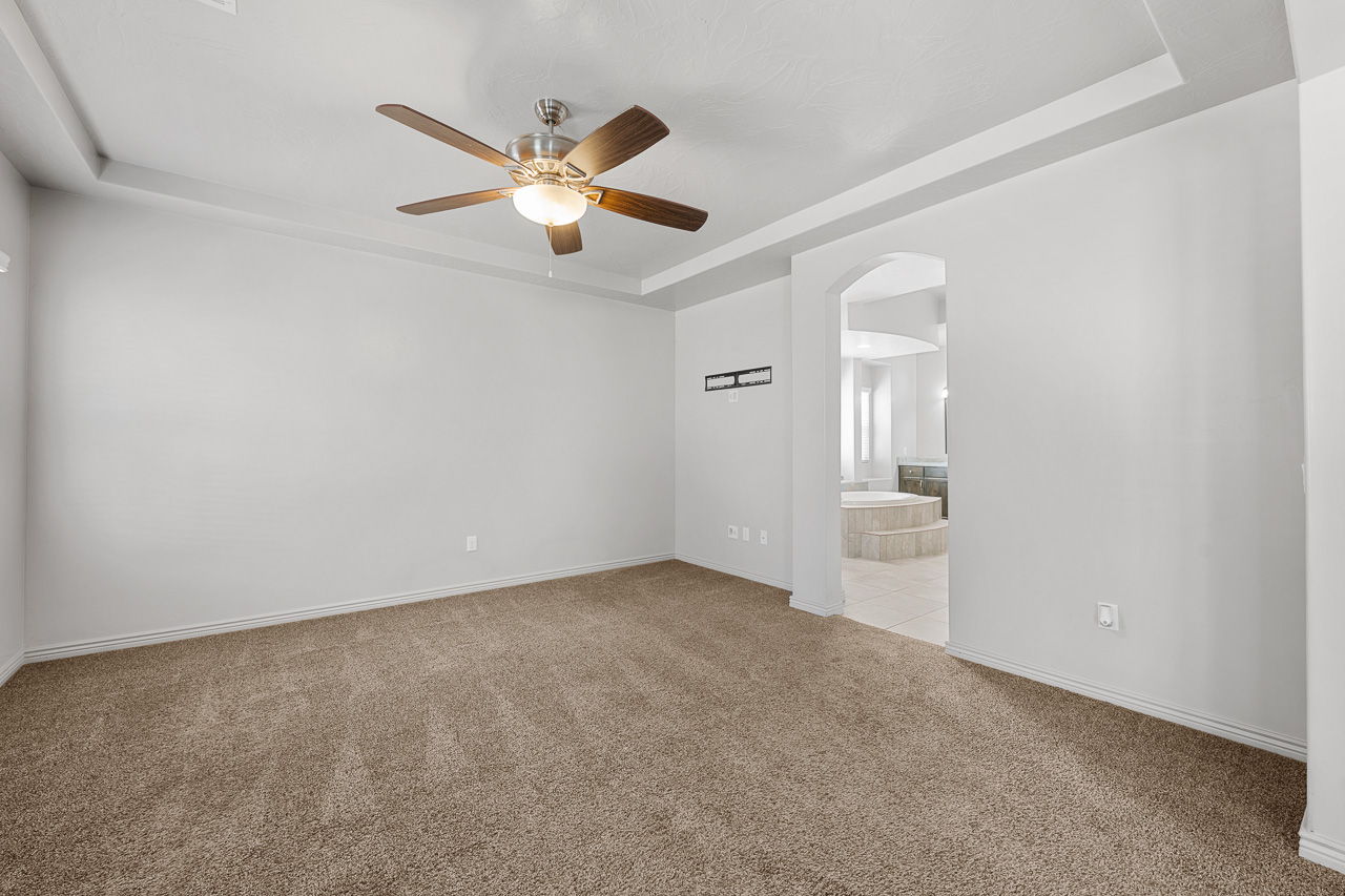 Empty room with a raised ceiling, light carpet, arched walkways, and ceiling fan