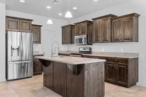 Kitchen featuring dark brown cabinetry, stainless steel appliances, a center island with sink, pendant lighting, and a breakfast bar