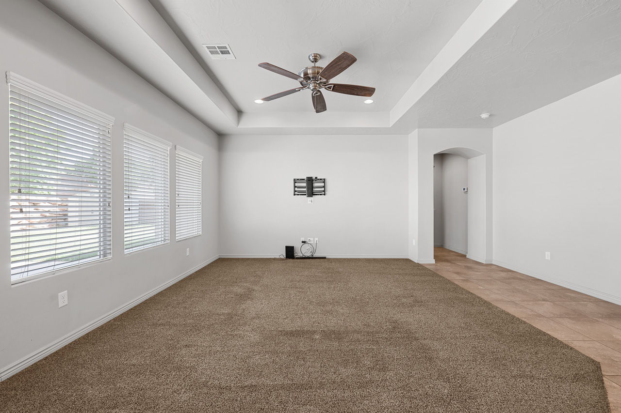 Unfurnished living room featuring arched walkways, a tray ceiling, light colored carpet, ceiling fan, and light tile patterned floors
