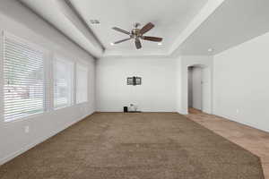 Unfurnished living room featuring arched walkways, a tray ceiling, light colored carpet, ceiling fan, and light tile patterned floors