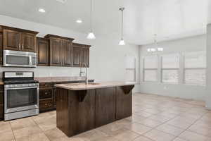 Kitchen with appliances with stainless steel finishes, hanging light fixtures, light tile patterned flooring, dark brown cabinets, and recessed lighting