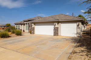 View of front of house with an attached garage, driveway, stucco siding, a tiled roof, and stone siding