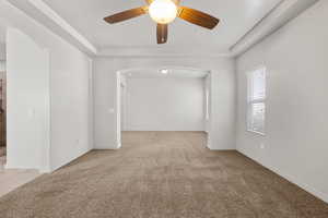 Unfurnished room featuring light carpet, arched walkways, a raised ceiling, and ceiling fan