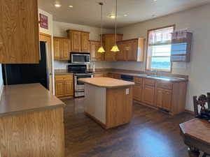 Kitchen with appliances with stainless steel finishes, decorative light fixtures, a center island, dark wood-type flooring, and a textured ceiling