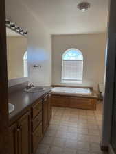 Full bath featuring a textured ceiling, a garden tub, double vanity, and light floors