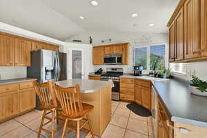 Kitchen with a kitchen bar, lofted ceiling, stainless steel appliances, a center island, and light tile patterned floors