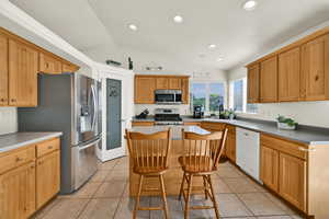 Kitchen featuring a kitchen breakfast bar, lofted ceiling, light tile patterned floors, appliances with stainless steel finishes, and recessed lighting