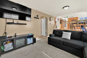 Carpeted living area with arched walkways and a textured ceiling